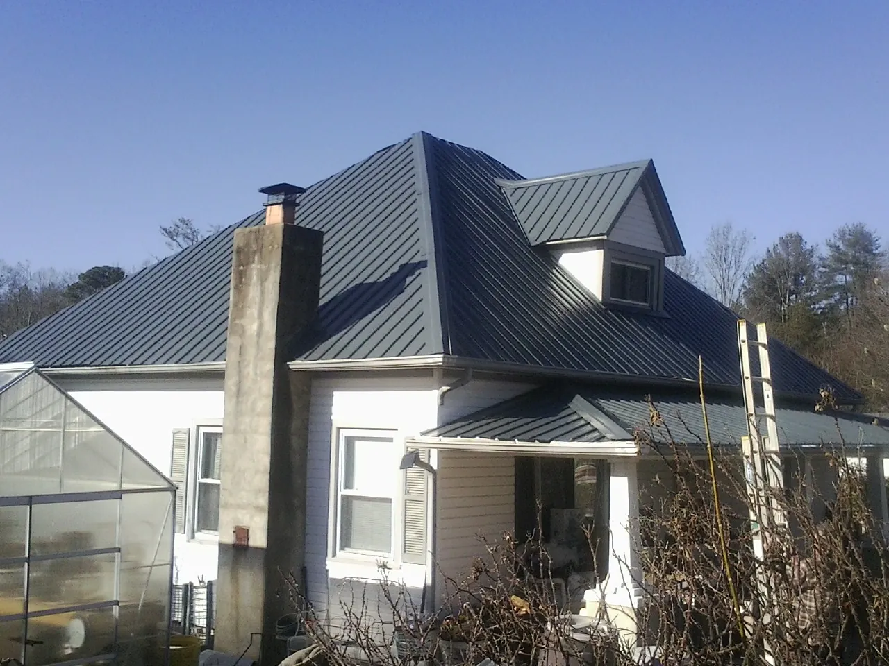 Dark blue standing seam metal roof on a white farmhouse with dormer — Slate & Tile Roof Repair by Roofing Brothers in Sandpoint