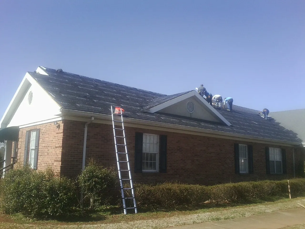 Crew tearing shingles off a brick ranch roof with a ladder set — Emergency Roof Repair work by our crew in Sandpoint