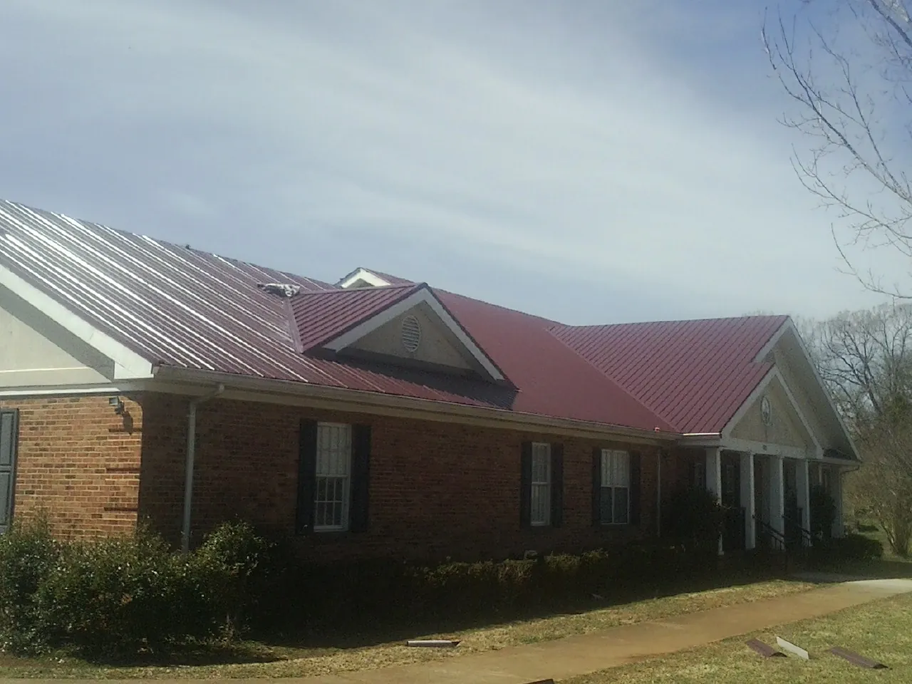 Red metal roof with gabled entries on a long brick building, from a Hail Damage Roof Repair job in Sandpoint