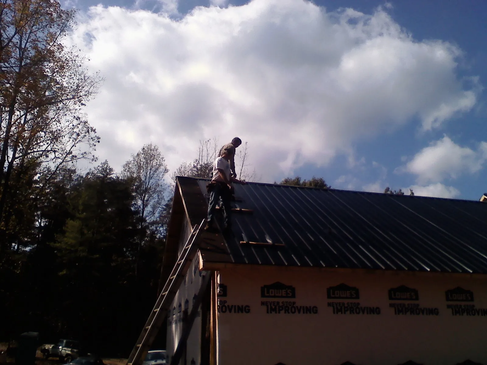 Roofer fastening dark metal panels high against a cloudy sky, from a Roof Inspection job in Sandpoint